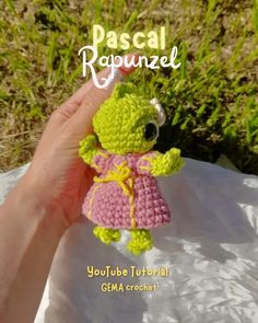 a small crocheted doll in a pink dress is being held by someone's hand