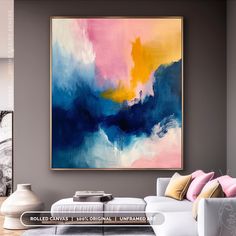 an abstract painting hangs on the wall above a white couch in a living room with pink, blue and yellow accents