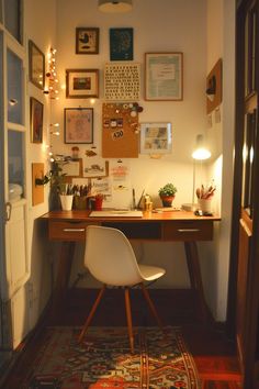 a room with a desk, chair and many pictures on the wall above it is lit by lights