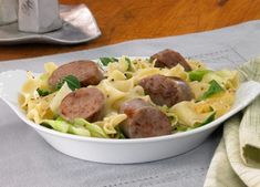 a white bowl filled with pasta and meat on top of a table next to a napkin