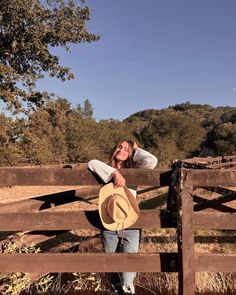 a woman leaning on a fence with a cowboy hat