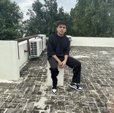 a young man sitting on top of a white wall next to a brick floor covered in dirt