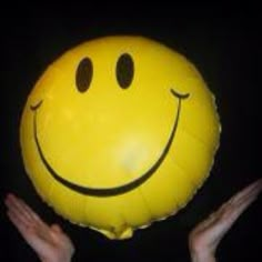 a yellow smiley face balloon being held up by someone's hands in the dark