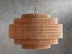 a large woven light fixture hanging from a metal chain on a gray wall with concrete flooring