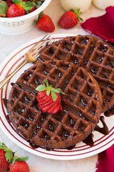 two waffles on a plate with chocolate sauce and strawberries next to them