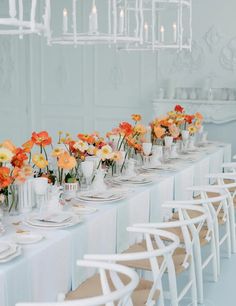 a long table is set with white chairs and flowers in vases on the tables