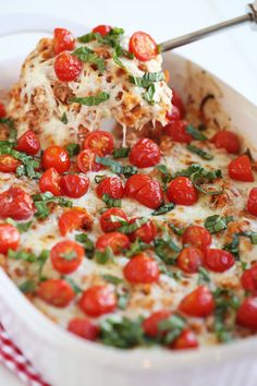 a casserole dish with tomatoes and cheese being lifted from the casserole