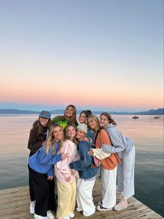 a group of women standing on top of a wooden pier next to the ocean at sunset