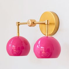 a pair of pink and gold wall lights on a white wall with a circular light fixture