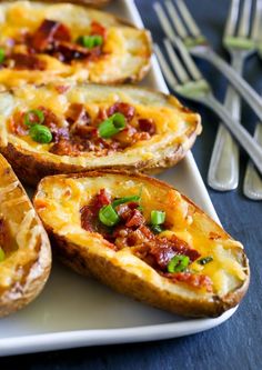 baked potatoes with bacon and green onions on a white platter next to silverware