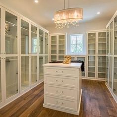 a large walk in closet with lots of glass doors and drawers on both sides, along with a chandelier hanging from the ceiling