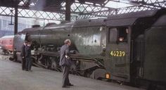 two men in suits are standing next to an old fashioned train at the station while another man looks on