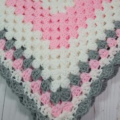 a crocheted blanket with pink, grey and white squares on top of it