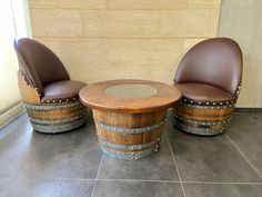 two brown leather chairs sitting next to each other on top of a tile floor near barrels