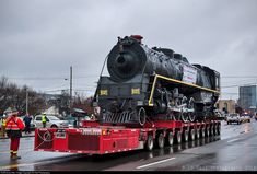 a large black train on a flatbed trailer in the middle of a city street