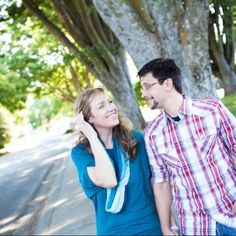 a man and woman standing next to each other on the side of a tree lined street