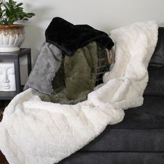 a black couch with blankets on it and a potted plant in the corner next to it