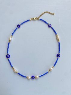 Protect yourself in style with our stunning Evil Eye beaded necklace. This piece combines the mystical charm of the evil eye symbol with the elegance of freshwater pearls and the vibrant beauty of blue seed beads and gold beads. Crafted with durable stainless steel, this necklace is both waterproof and tarnish-resistant, ensuring lasting beauty and protection. Key Features: Evil Eye Charm: Symbolizing protection and warding off negativity, the evil eye charm adds a meaningful touch to this beautiful necklace. Freshwater Pearls: Genuine freshwater pearls provide an elegant and timeless appeal. Blue Seed Beads: Vibrant blue seed beads enhance the necklace's aesthetic and add a pop of color. Gold Beads: High-quality gold beads offer a luxurious touch. Stainless Steel: Made with durable stainl White Evil Eye Beaded Necklace, Spiritual Beaded Necklace With Pearl Charm As Gift, Handmade Pearl Beaded Necklaces For Festivals, Handmade Pearl Beaded Necklace For Festivals, Spiritual Pearl Beaded Necklaces With Round Beads, Blue Pearl Necklaces With Colorful Beads, Spiritual Beaded Pearl Necklace With Round Beads, Spiritual Pearl Beaded Necklace With Round Beads, Adjustable Pearl Beaded Necklace With Spacer Beads