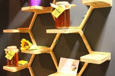 honey jars are arranged on hexagonal shelves in front of a wall with flowers