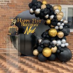 a black and gold balloon arch with the words happy 21st birthday next to it in front of a brick building