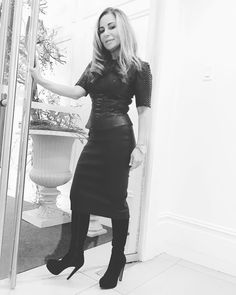 a woman standing in front of a mirror wearing high heeled boots and a black dress