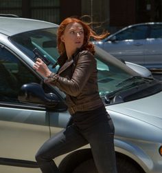 a woman in black jacket and jeans leaning on a car with her arm out to the side