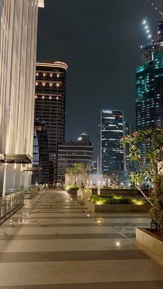 an empty walkway in the middle of a city at night with tall buildings behind it