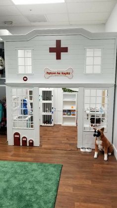 a dog sitting in front of a play house with a red cross on the roof