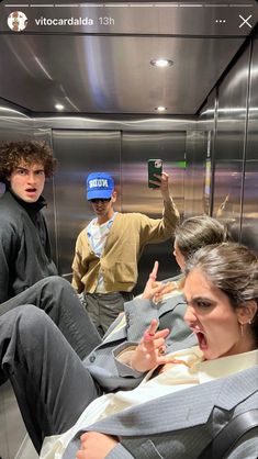 two men and a woman sitting in an elevator with one man pointing at his phone