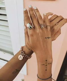 two women's hands with tattoos and rings on their wrists, both holding each other