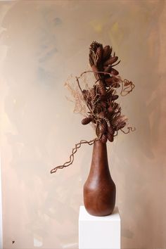 a brown vase with flowers in it on top of a white pedestal next to a wall