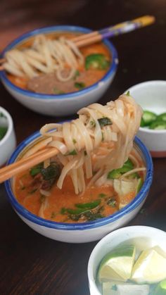 two bowls filled with soup and chopsticks on top of a wooden table,