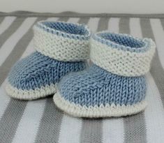 a pair of blue and white knitted baby booties sitting on a striped blanket