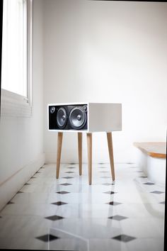 a white speaker sitting on top of a wooden table next to a black and white checkered floor