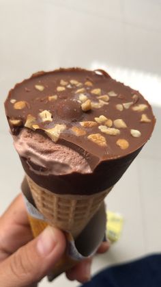 a hand holding an ice cream cone with chocolate and nuts