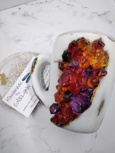 a white bowl filled with lots of different colored rocks on top of a marble counter