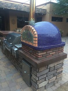 an outdoor bbq grill with blue glass tiles on the top and side wall, surrounded by brick pavers