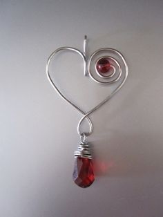 a heart shaped pendant with a red stone hanging from it's side on a white surface