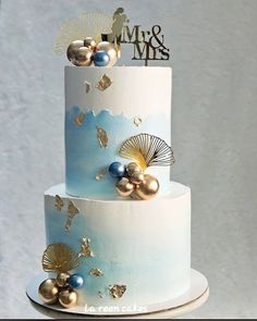 a three tiered blue and white wedding cake with gold decorations on the top layer