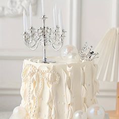 a wedding cake with white frosting and crystal candlesticks on top, sitting on a table next to a lamp