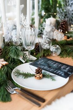 the table is set with pine cones, evergreen branches and candles for an elegant christmas dinner