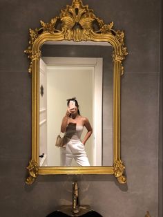 a woman taking a selfie in front of a gold framed mirror on the wall