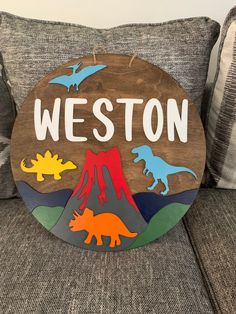 a wooden sign that says, weston with dinosaurs on the front and mountains in the back