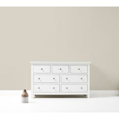 a white dresser against a pink wall with a vase on the floor next to it