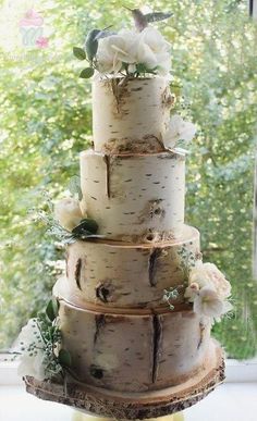 a three tiered cake with white flowers and leaves on the top is sitting in front of a window