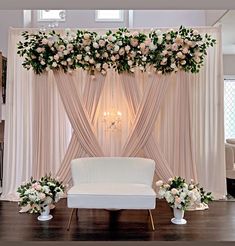 a white couch sitting in front of a wall with flowers on it and greenery hanging from the ceiling