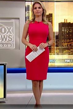 a woman in a red dress is standing on the news desk with her hand up to her chest