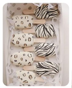 several popsicles decorated with animal print and wooden sticks in a white box on a polka dot tablecloth