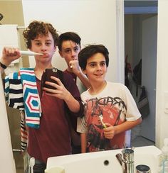 three boys brushing their teeth in front of the bathroom mirror while taking a selfie