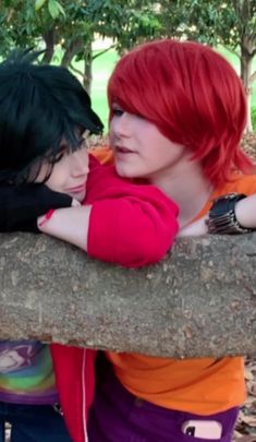 two young women with red hair are hugging each other on a tree branch in the park